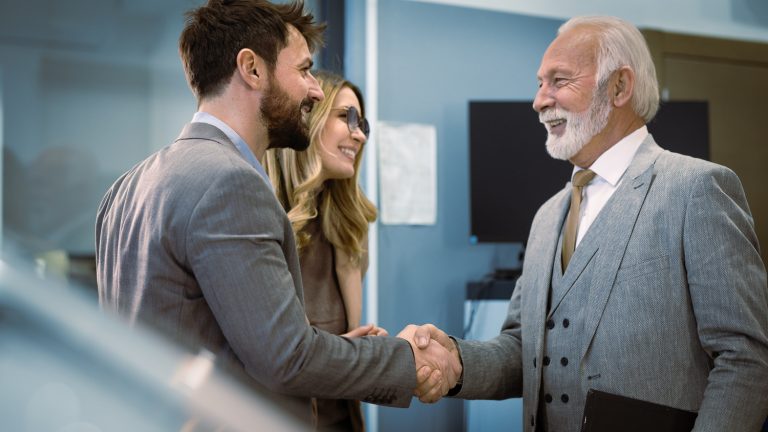 Married couple shakes hands with car salesperson after they have purchased their new vehicle