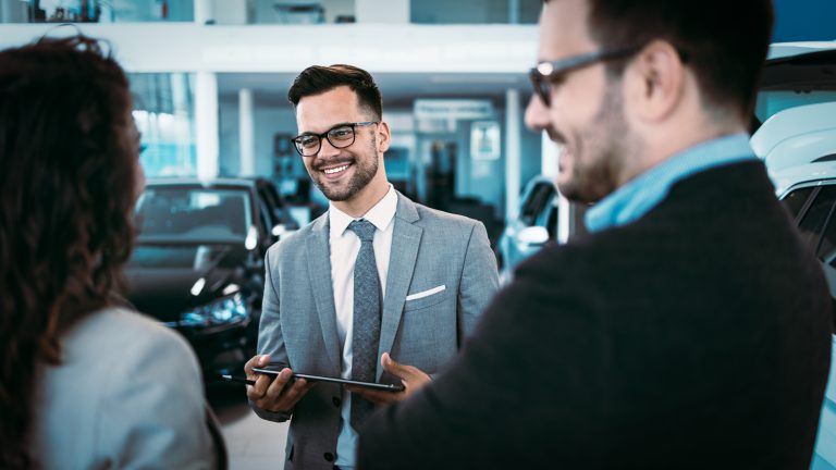 Middle age couple choosing and buying car at car showroom. Car salesman helps them to make right decision.
