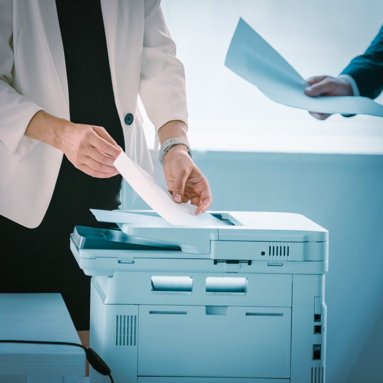 businesswoman talking on smartphone while using printer in office with colleague near by